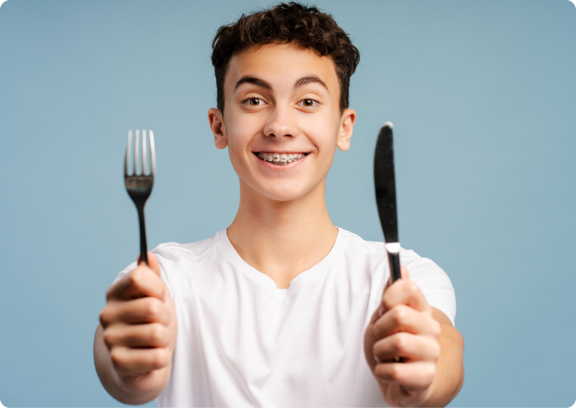Adolescent souriant tenant une fourchette et un couteau